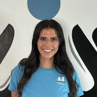 Office Manager Shelby Gonzales Smiling In Front Of Logo Wall