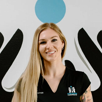 Chiropractor Jenna Swaffer Smiling In Front Of Logo Wall